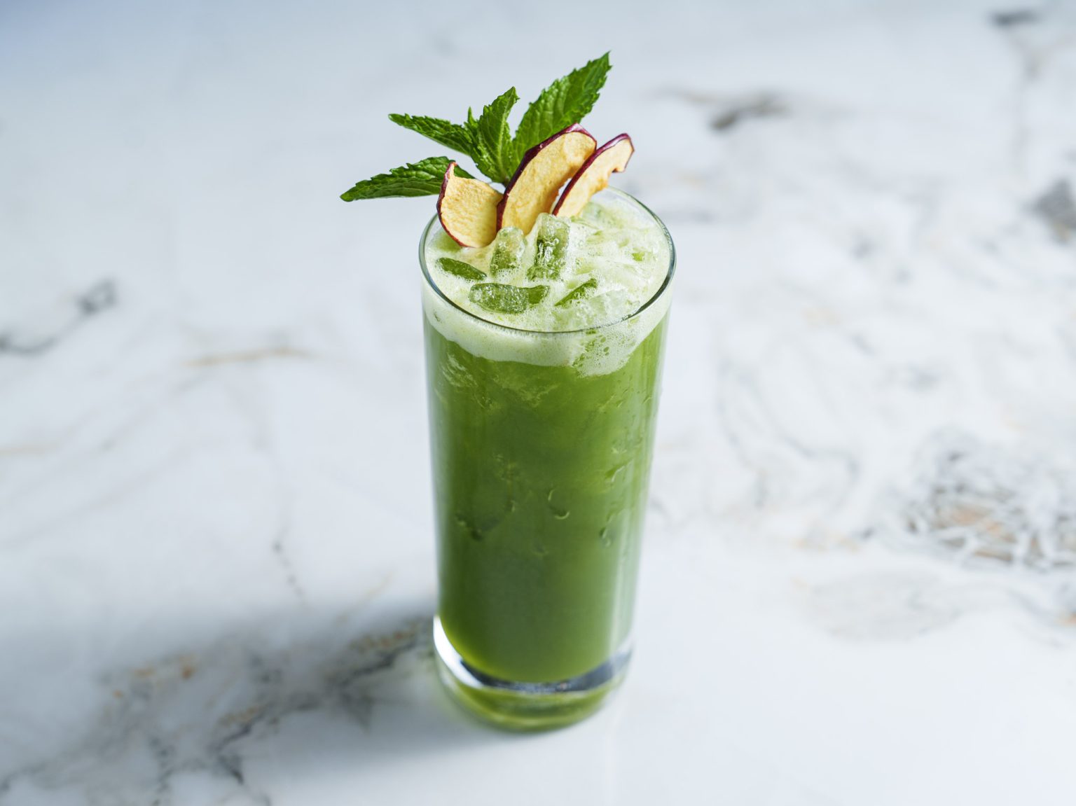 Order refreshing iced green juice garnished with fresh mint and apple slices in a tall glass.